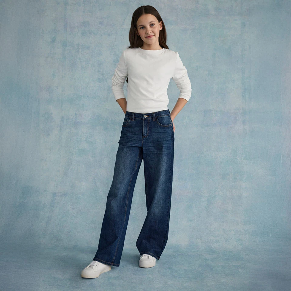 Biała, teksturowana góra połączona z szerokimi dżinsami i białymi sneakersami.