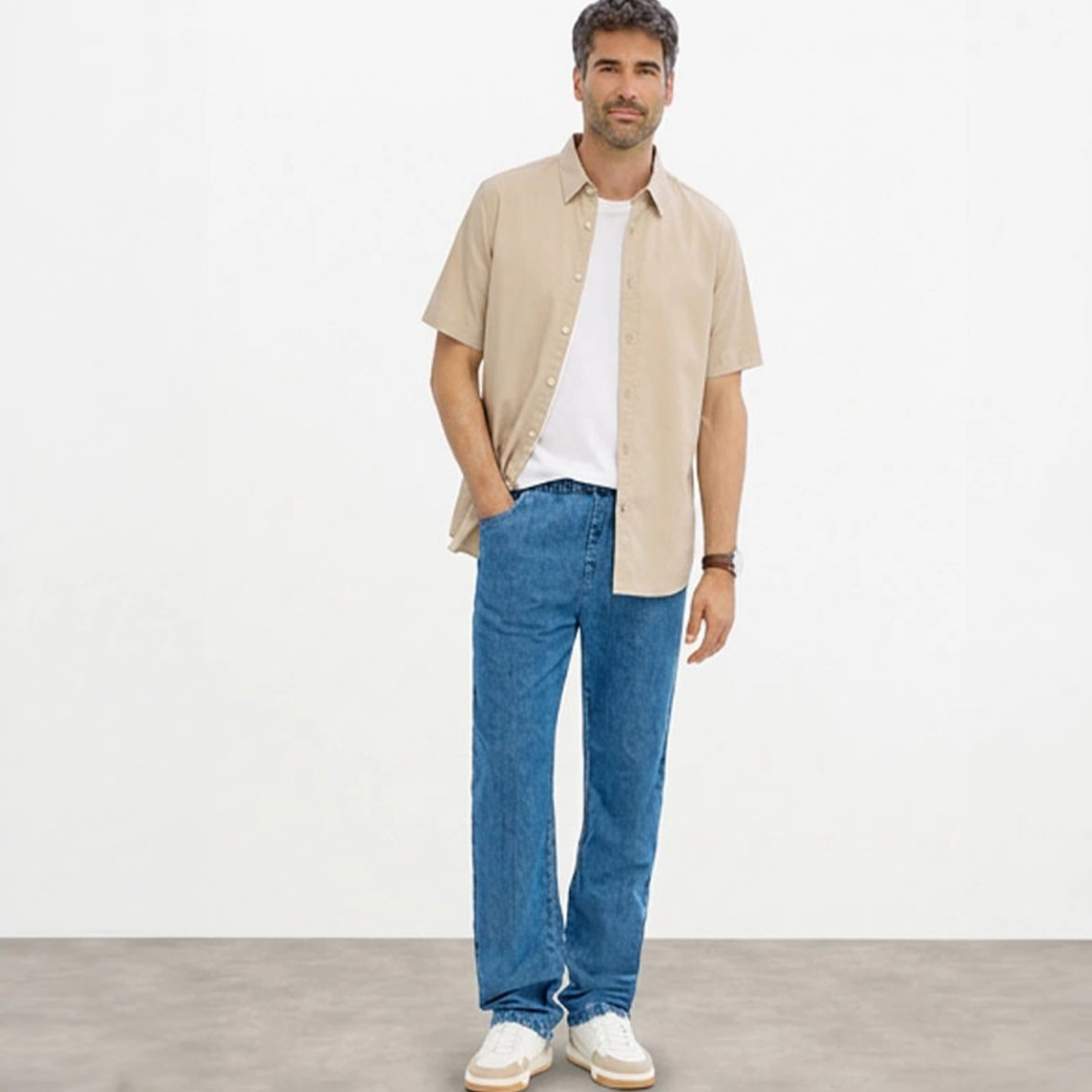 Beżowa koszula z krótkim rękawem, biały T shirt, niebieskie jeansy o kroju Classic Fit i białe sneakersy.