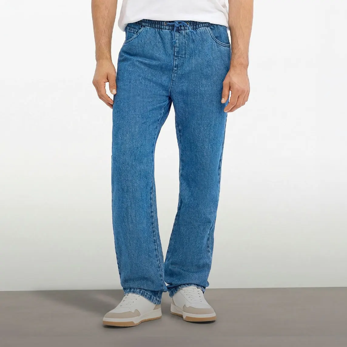 Beżowa koszula z krótkim rękawem, biały T shirt, niebieskie jeansy o kroju Classic Fit i białe sneakersy.