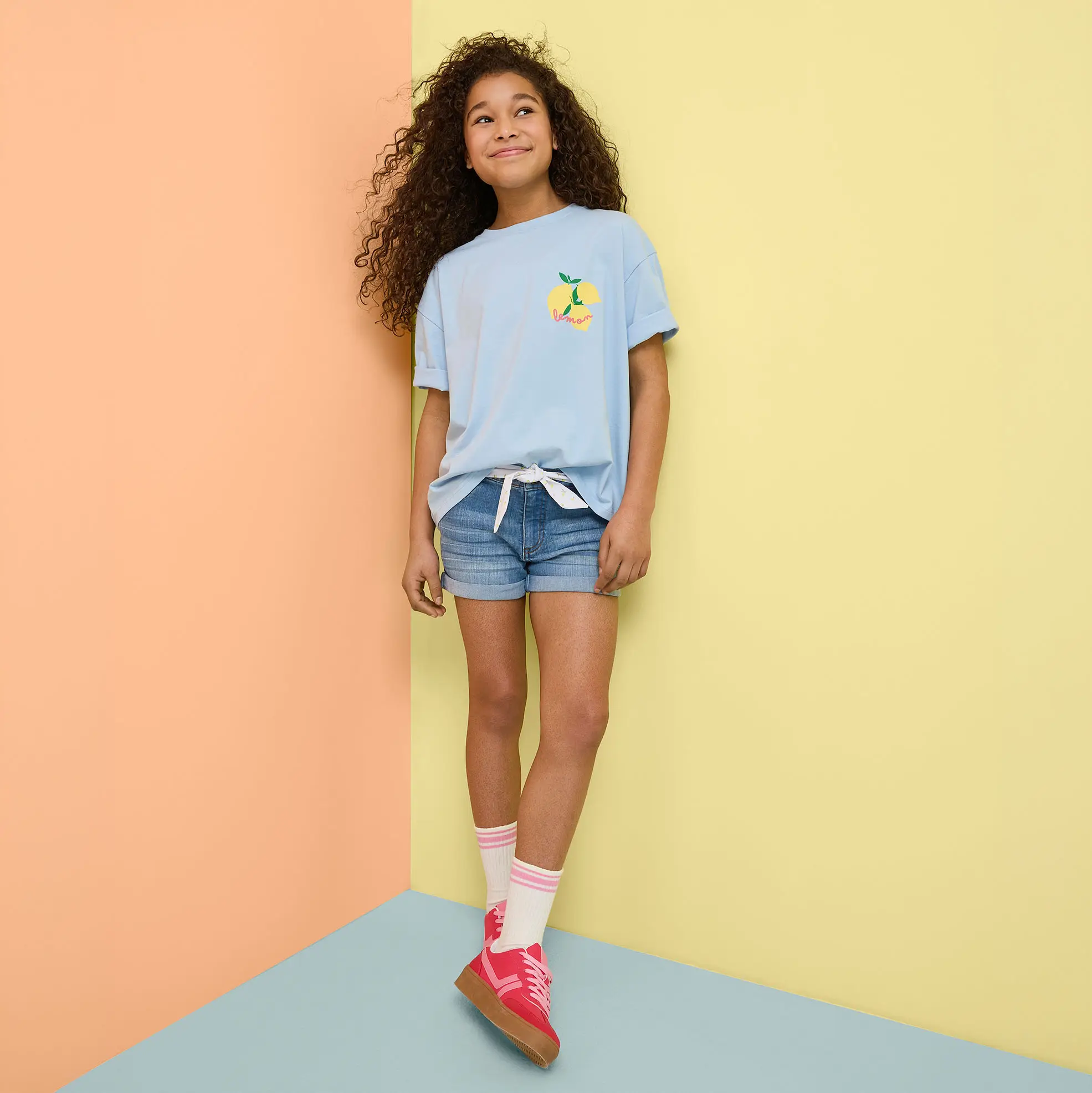 Letnia stylizacja: jasnoniebieski T-shirt, jeansowe szorty i kolorowe sneakersy.